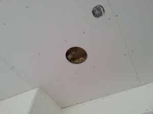 Hole cut in drywall to expose opening in containment box